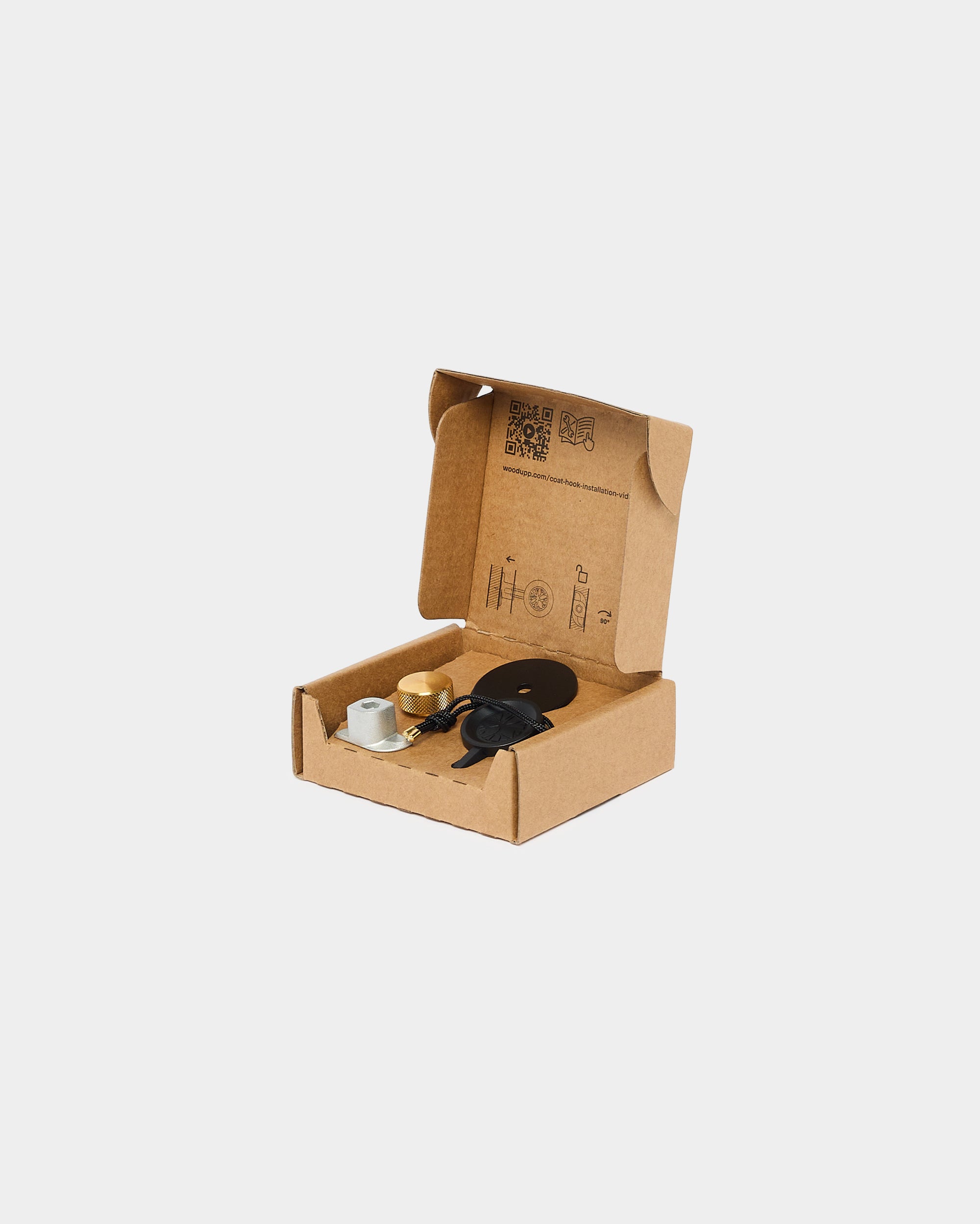 Coat hook mounting kit with brass knob, metal bracket and black cord in open cardboard box on plain white background